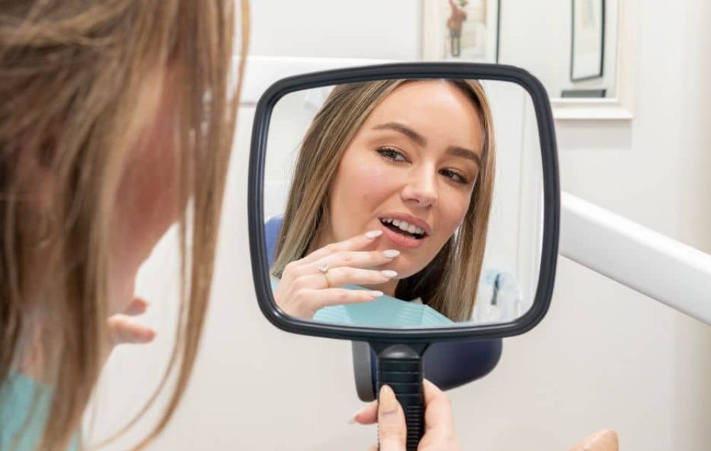 Woman holding a mirror checking her teeth.