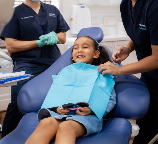 child sitting in dentist chair smiling while they prepare her for procedure