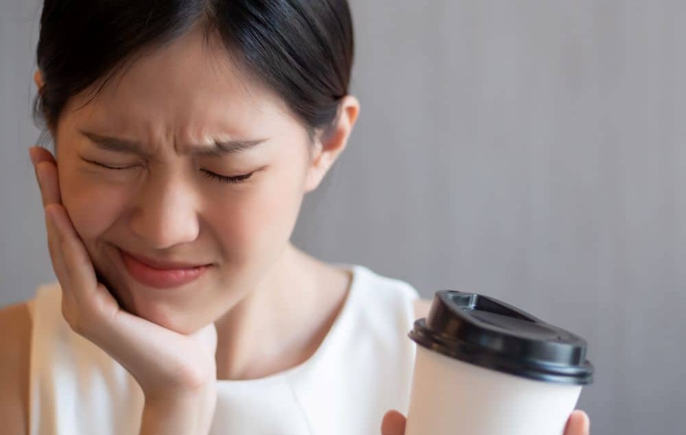 Woman with sensitive tooth experiencing pain while drinking coffee.